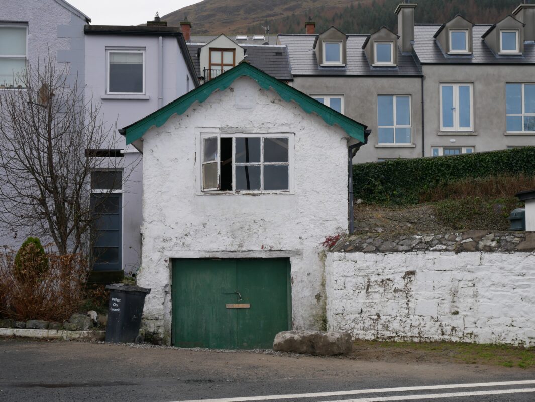 Small white building with green door and roof in Carlingford, Ireland